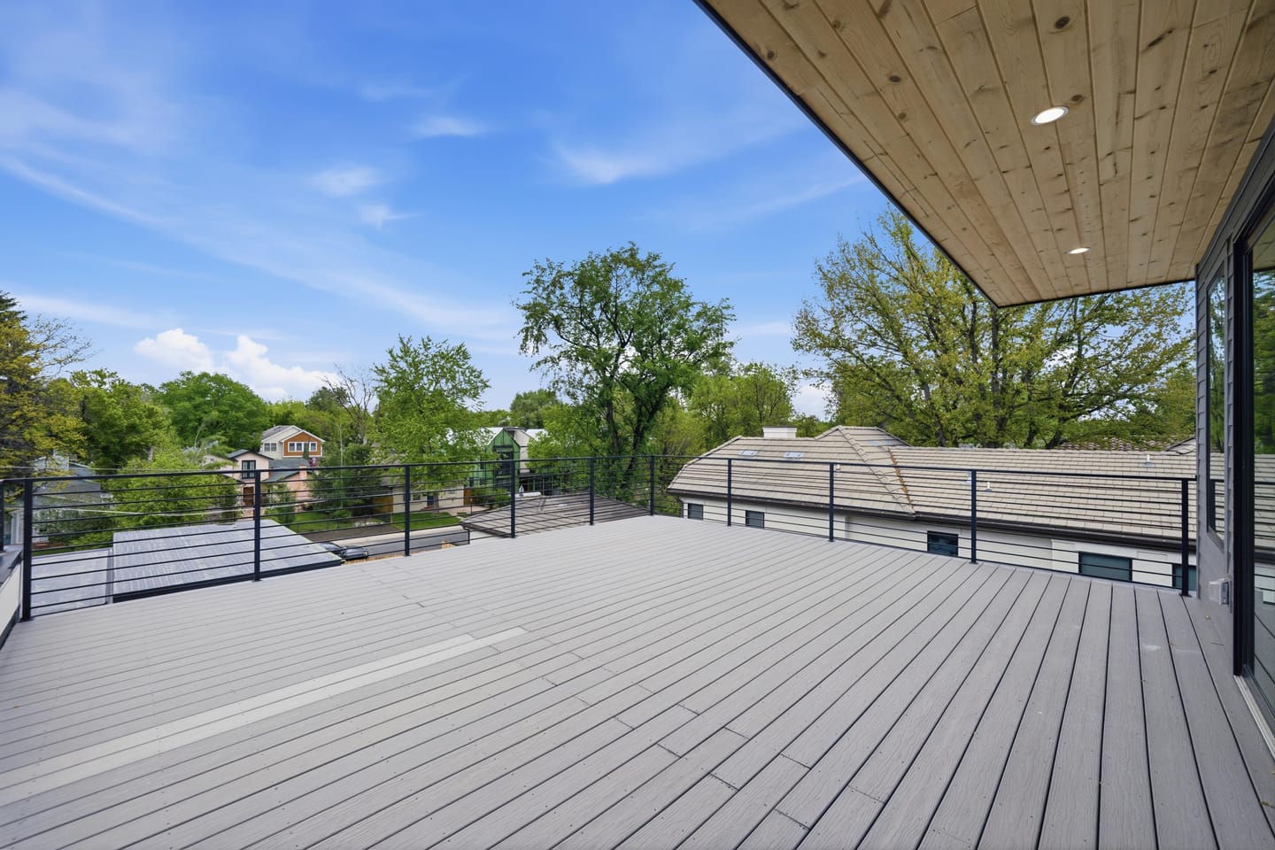 Rooftop deck with wood soffit and cable railing above the tree canopy