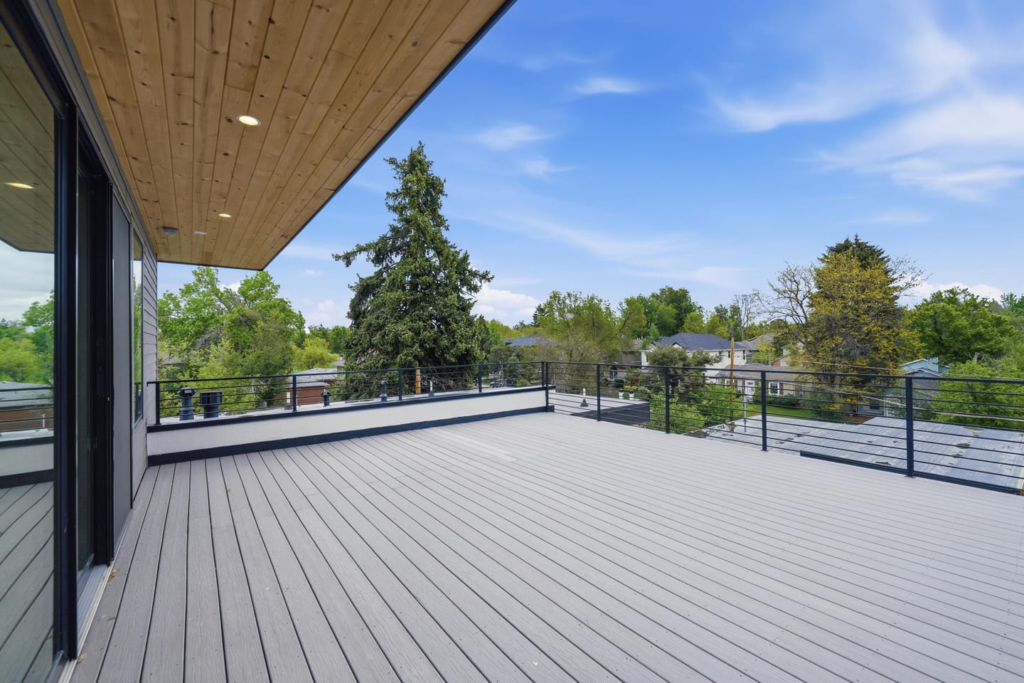Rooftop deck with wood soffit and cable railing above the tree canopy