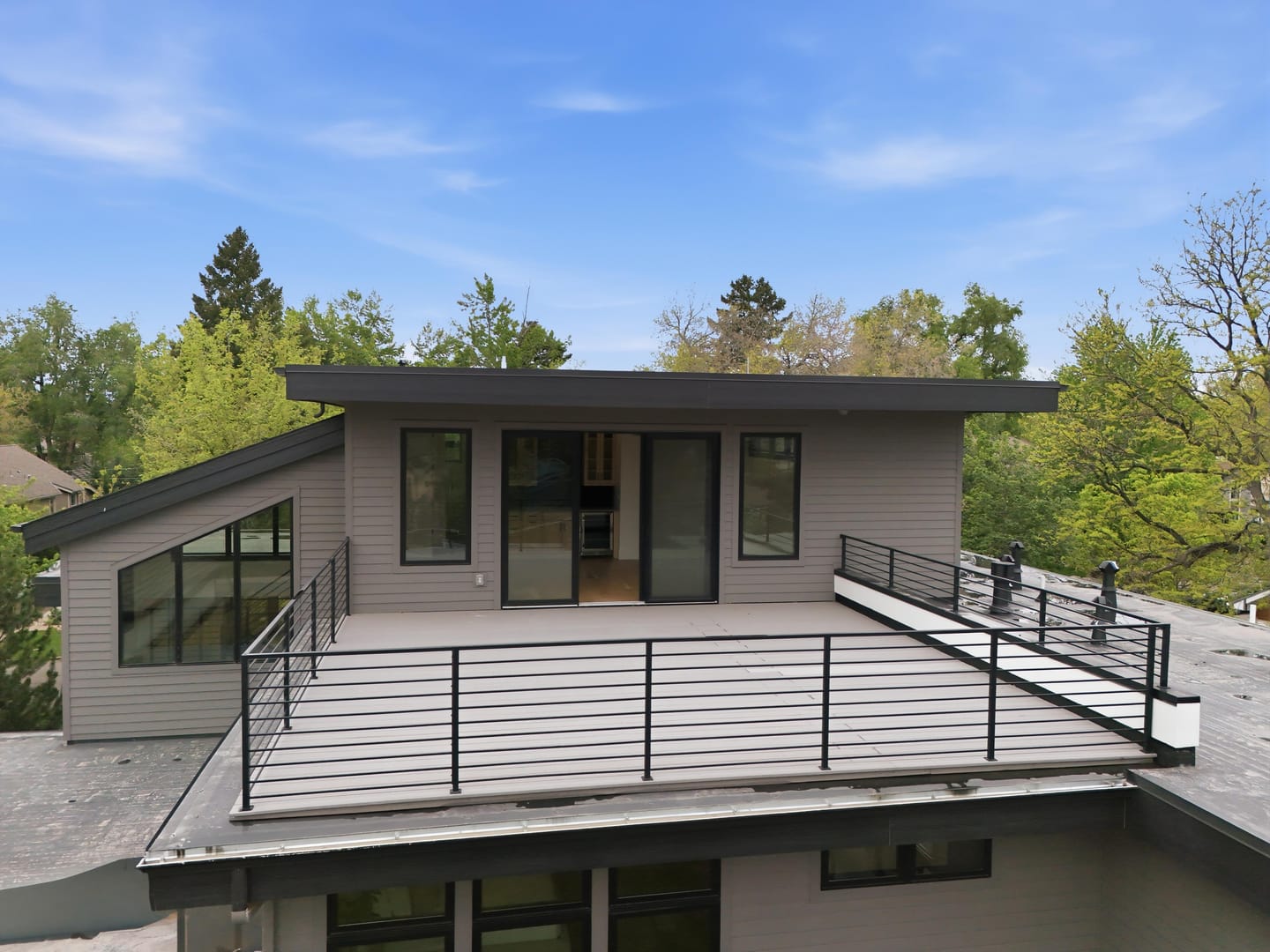 Rooftop deck with wood soffit and cable railing above the tree canopy
